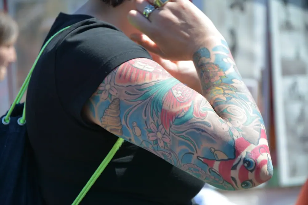 Braço com uma tatuagem grande e colorida em tons de vermelho, roxo e azul.